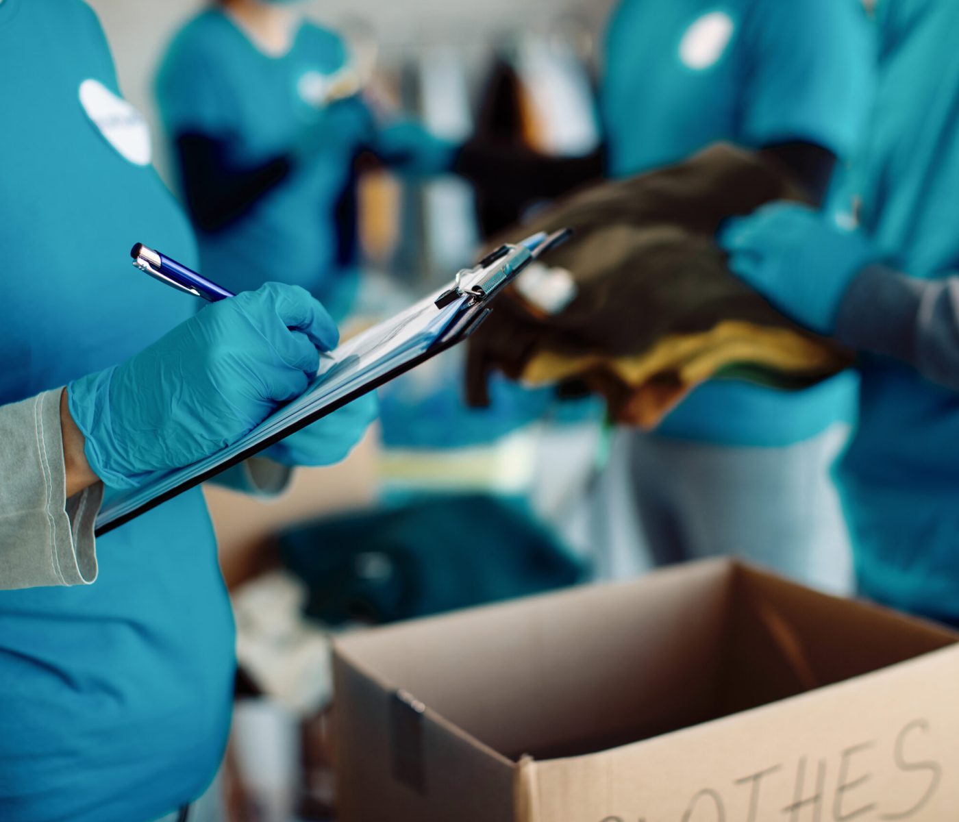 Close-up of woman taking notes while volunteers are packing donation boxes for charity.